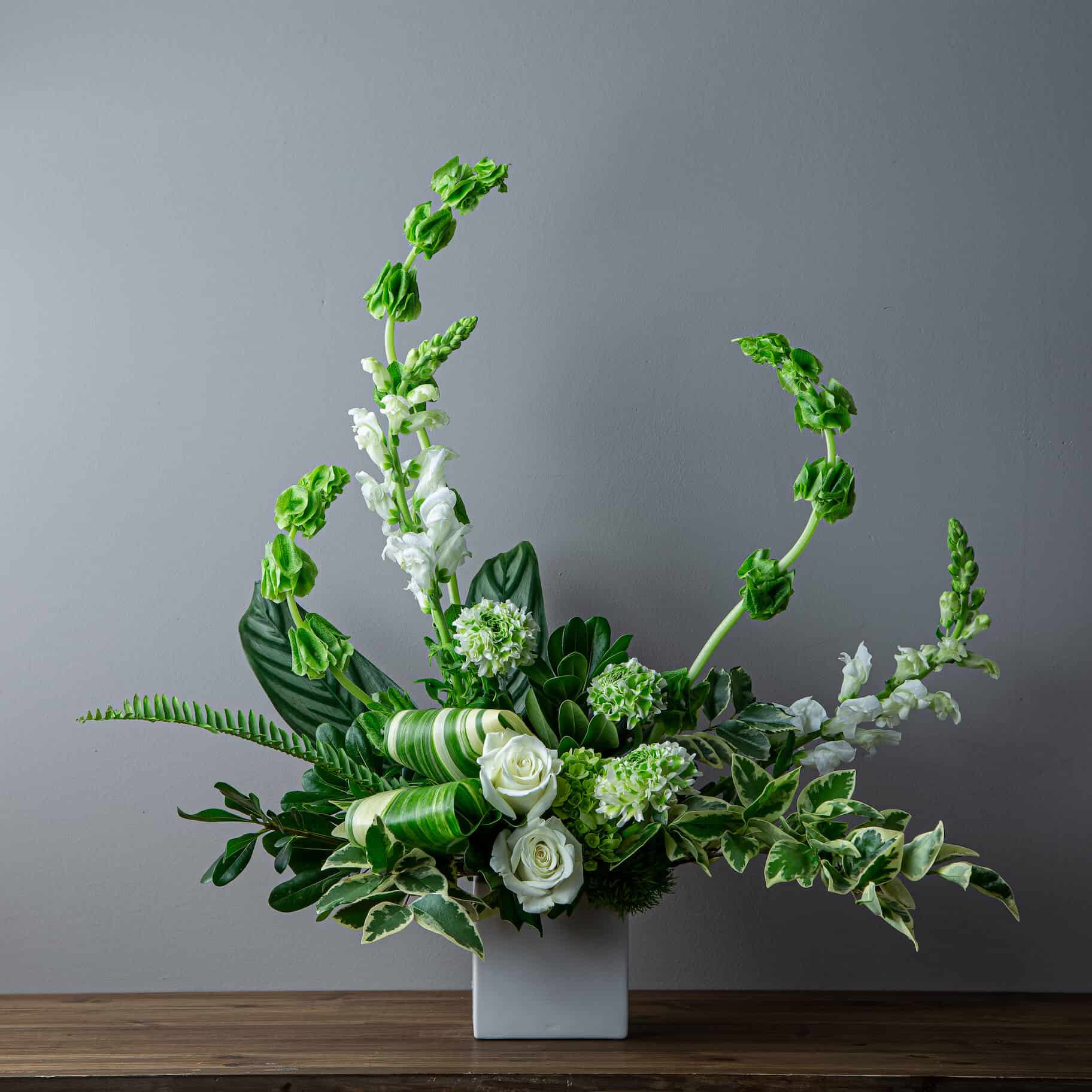 floral arrangement In a white vase with white and green Floral such as White roses, bells of Ireland, and white snapdragons , Ivory Florist offers same day flower delivery in Irvine Ca, best florist in irvine, Number one flower shop in irvine, florist near irvine